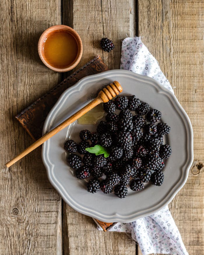 Rustic plate of fresh blackberries served with honey on a wooden table, top view.